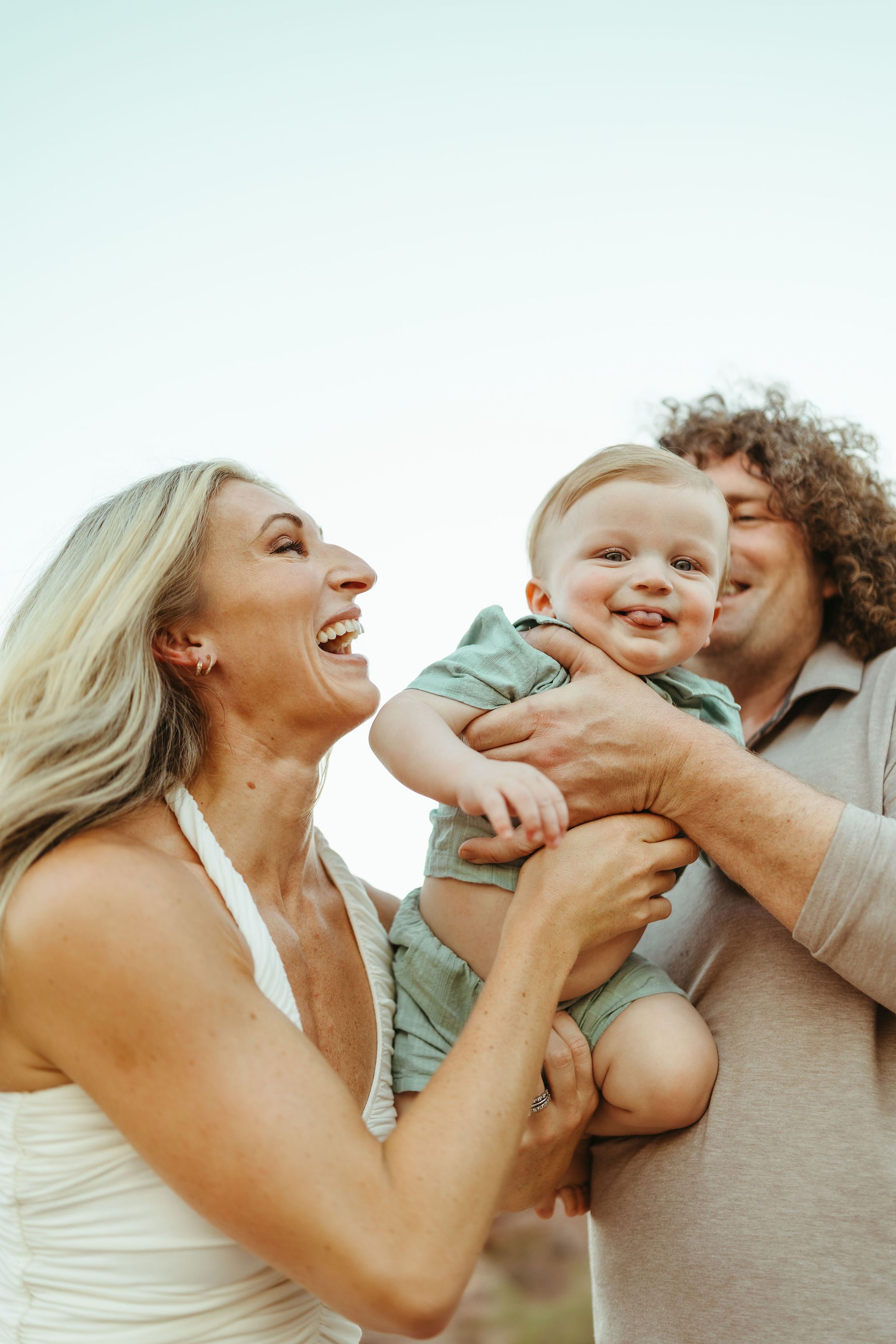 Gilbert family photography session featuring candid, emotional parent interactions and playful moments with a laughing baby boy at golden hour.