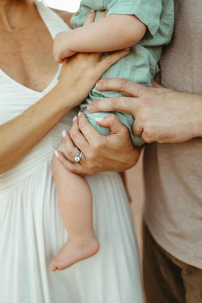 Paradise Valley family photographer highlighting a luxury detail shot of a mother's hands and elegant rings holding her baby during a desert session.