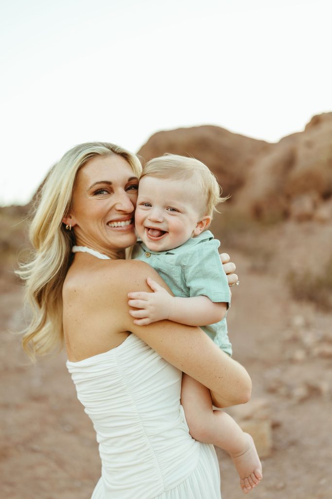 Mesa family photography featuring a sweet, unposed connection between a mother and her smiling baby boy against a warm desert mountain backdrop.