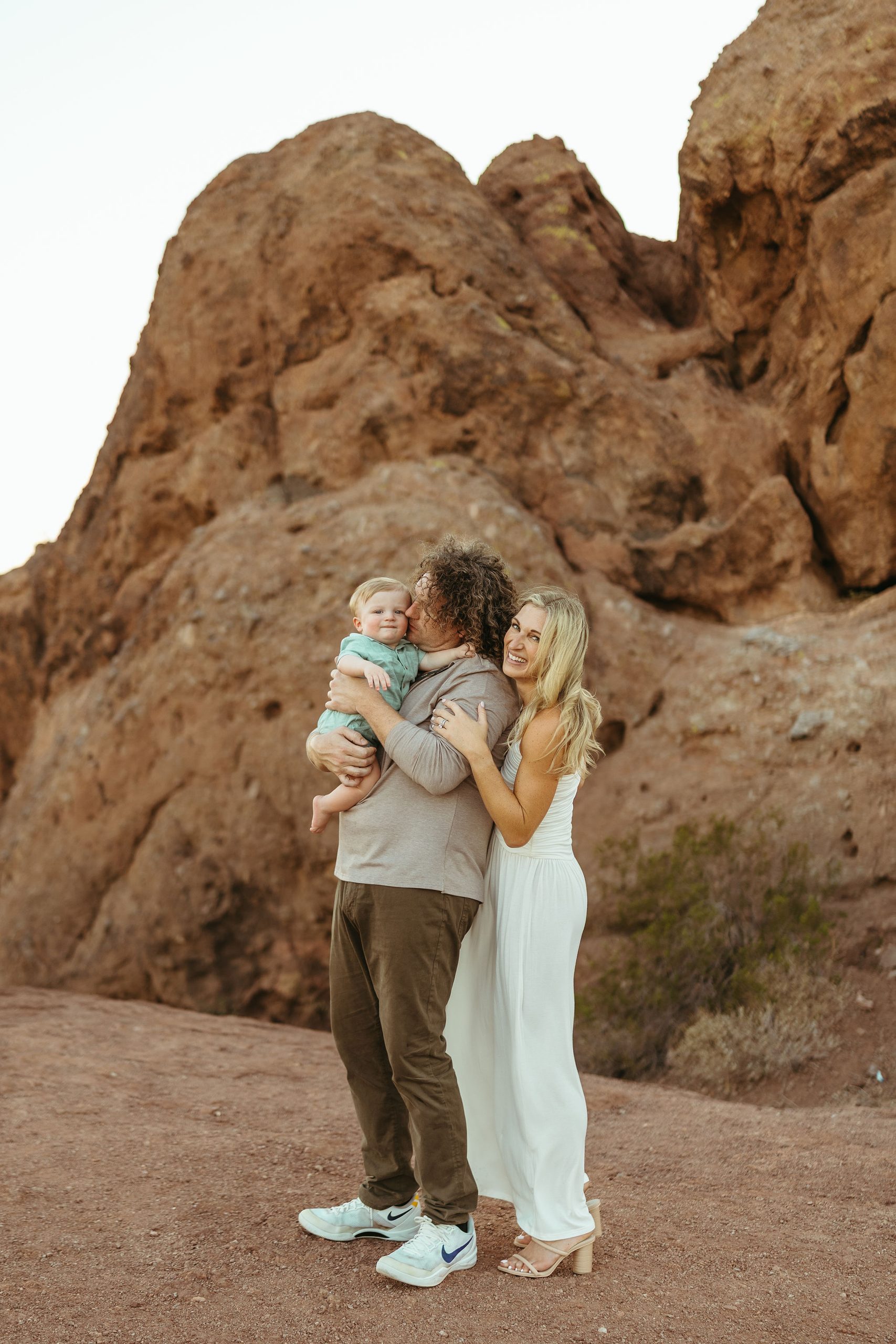 Mesa family photography showcasing an unposed, joyful moment as parents hold hands and walk with their baby boy along a palm tree-lined shore.