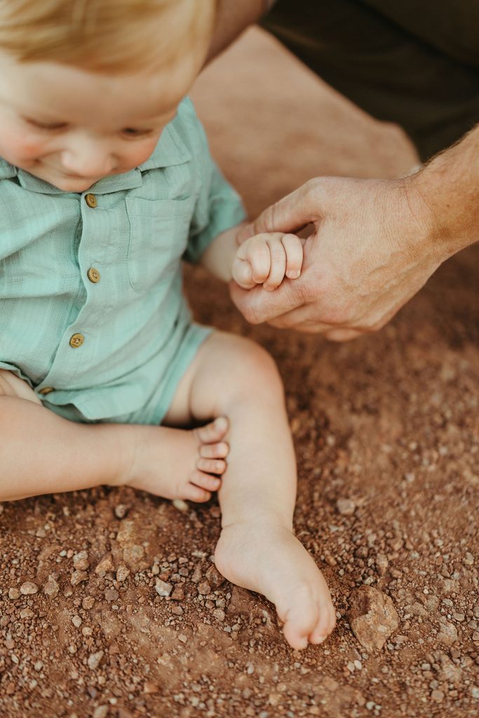 Paradise Valley family photographer highlighting a close-up lifestyle portrait of a baby boy holding his father's hand in the desert sand.