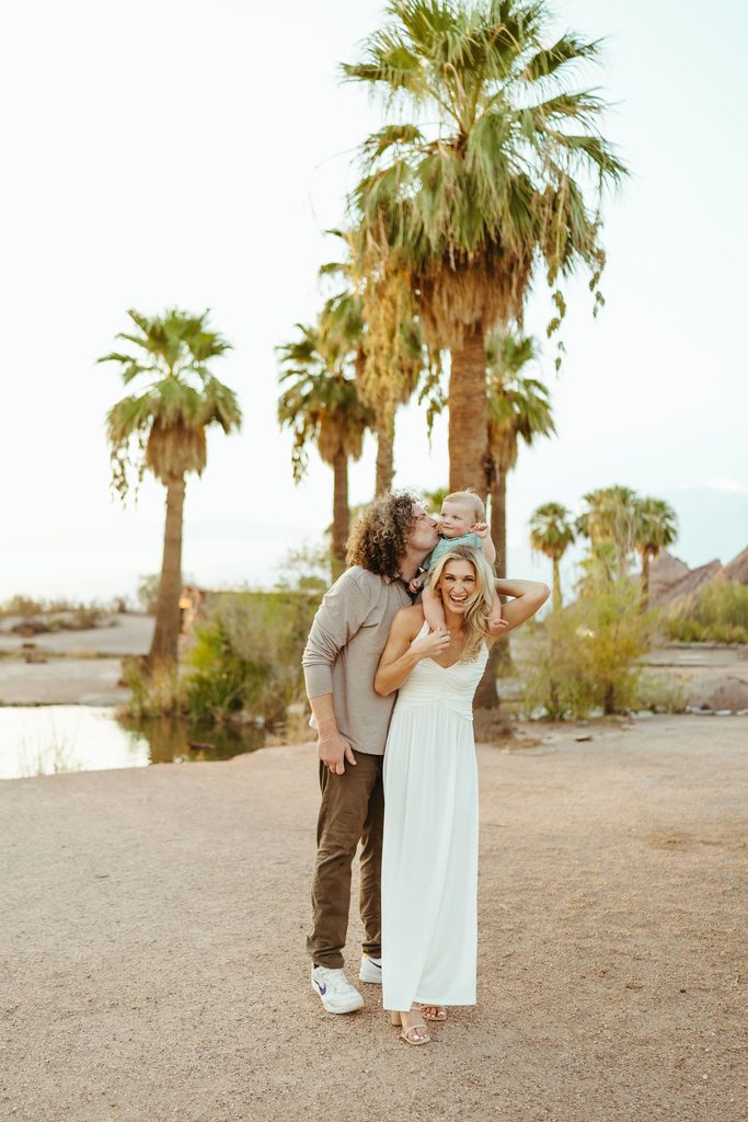 Phoenix family photographer capturing a playful golden hour portrait of a family standing by towering palm trees near the water at Papago Park.