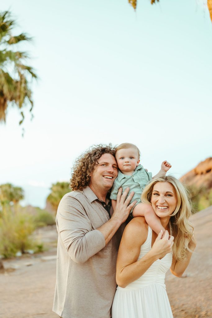 Gilbert family photography featuring an effortless, true-to-color portrait of a family of three laughing together during a scenic outdoor desert session.