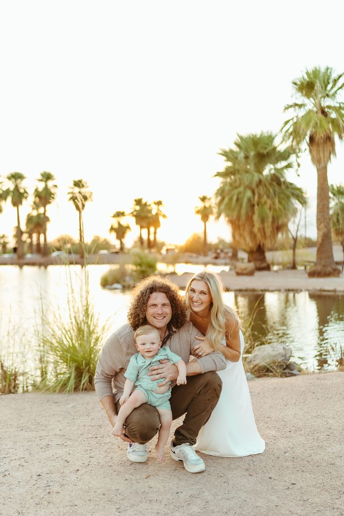 Queen Creek family photography documenting a sweet, candid family moment crouching together next to a desert oasis pond at sunset.