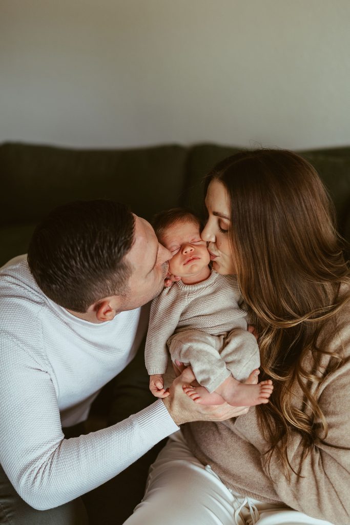 Scottsdale newborn photographer capturing parents lovingly kissing their newborn baby during a warm and intimate in-home newborn photography session in the Phoenix area.