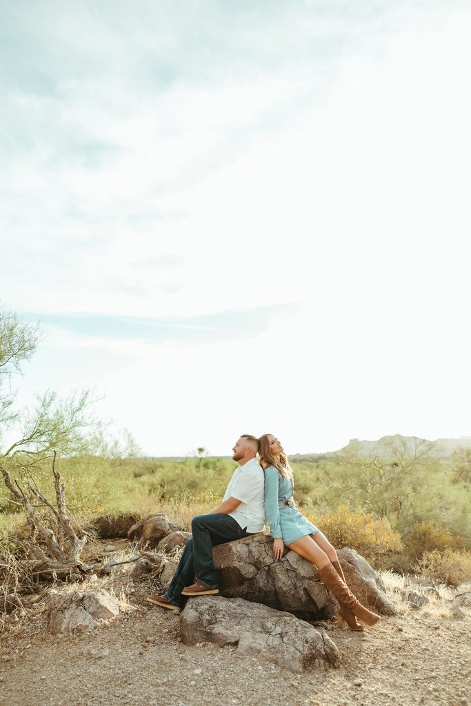 Superstition Mountains couples photographer capturing an intimate moment as an engaged couple sits together on desert rocks surrounded by Arizona cacti.