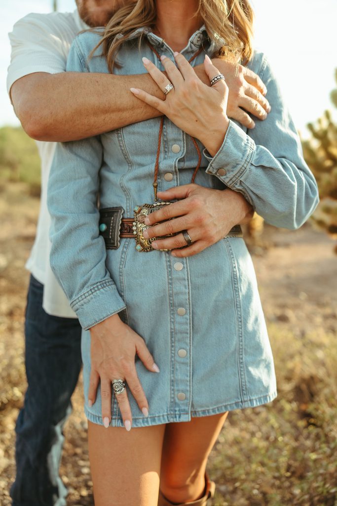 Arizona couples photographer capturing an intimate close-up of an engaged couple embracing in the desert, with the woman's engagement ring visible against her fiancé's arms.