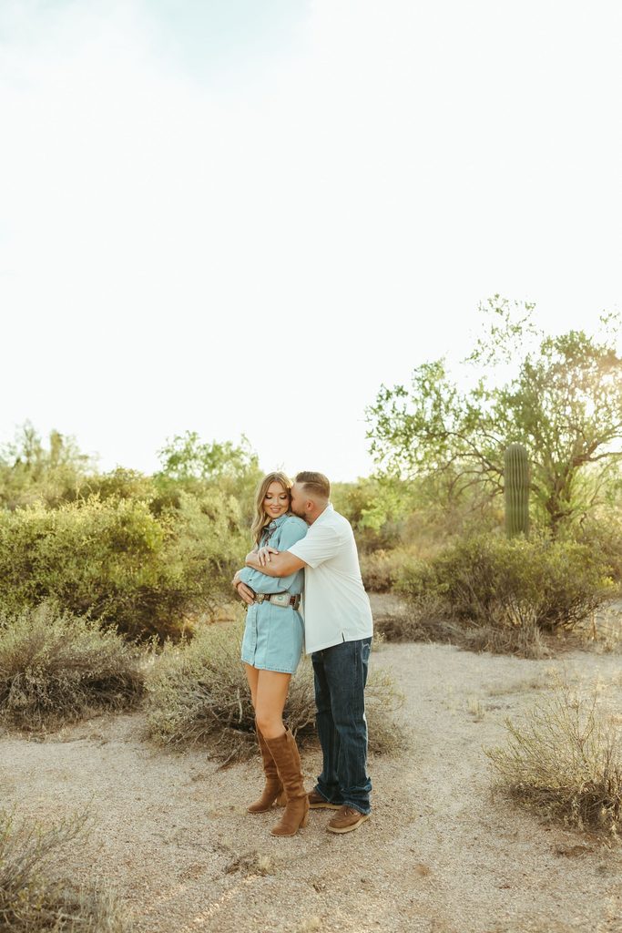 Superstition Mountains engagement photos of a couple embracing on a desert trail surrounded by Arizona greenery and cacti.