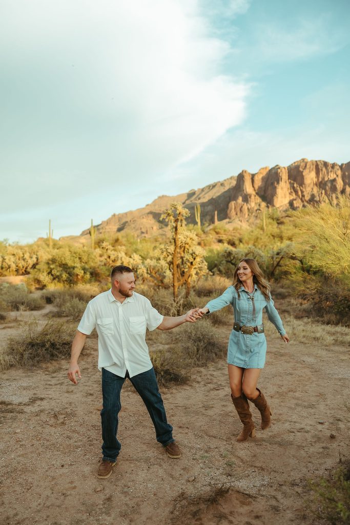 Superstition Mountains engagement photographer capturing a couple walking hand in hand through the Arizona desert with dramatic mountain views behind them.