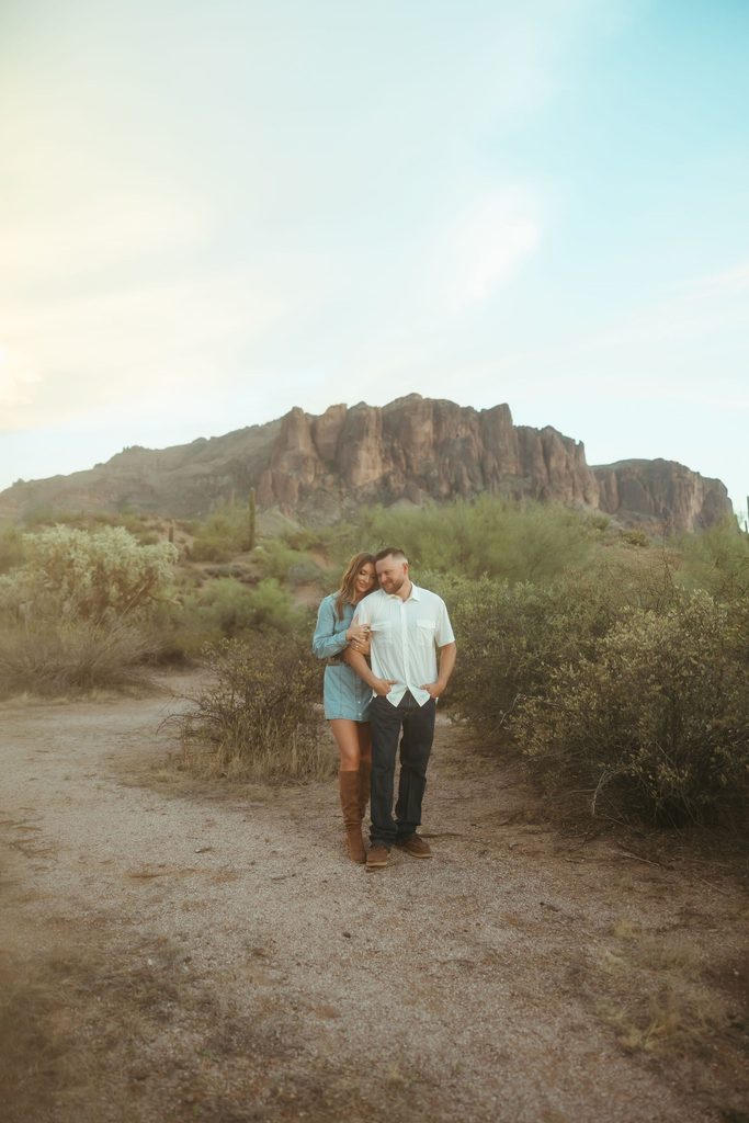 Arizona engagement photos of a couple walking together through the desert with the Superstition Mountains creating a dramatic backdrop.