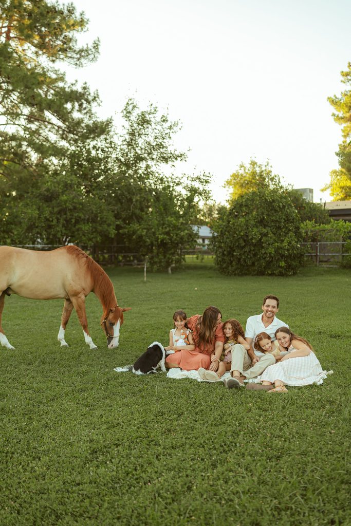 Luxury family photography in Gilbert featuring parents and children gathered together in a sunlit pasture with their horse nearby.