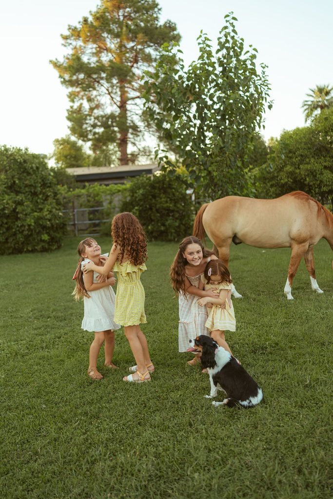 Gilbert family photography featuring sisters playing together with their dog and horse during a golden hour session at Floyd Family Farms.