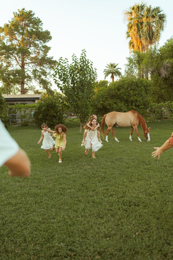 Gilbert family photographer capturing children running through the pasture with their horse during a playful golden hour family session at Floyd Family Farms.