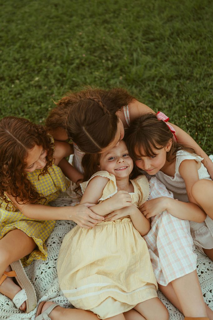 Gilbert family photography capturing four sisters cuddling together on a blanket during a relaxed outdoor family session at Floyd Family Farms.