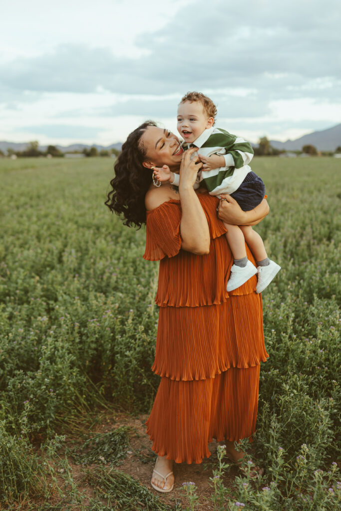 Mom and dad cuddling their toddler in a green field during family photos in Queen Creek, Arizona