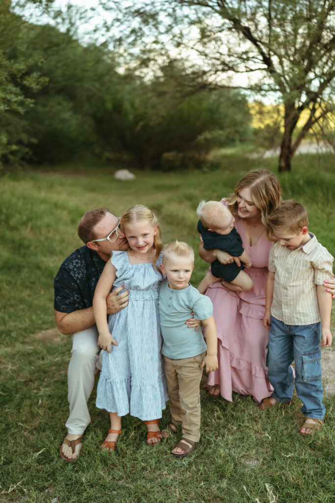 Parents sharing sweet candid moments with their four young children during an outdoor family photo session at Butcher Jones in Mesa, AZ.