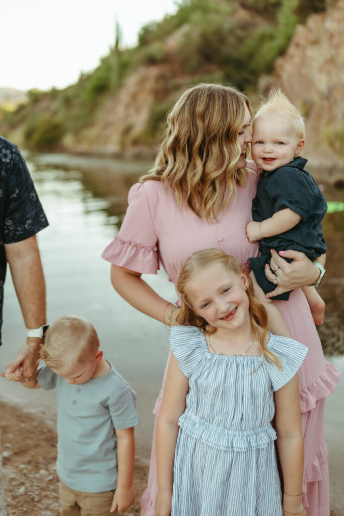 Mother holding her baby boy alongside his siblings during a candid family photography session at Butcher Jones near Saguaro Lake in Mesa, Arizona.