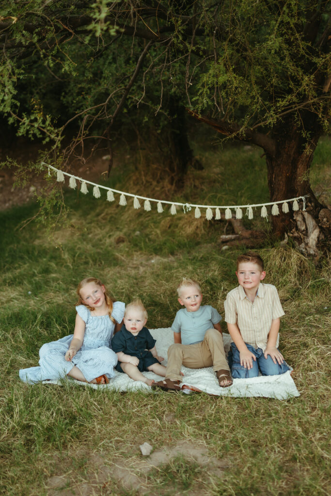 Four siblings posing together on a blanket during a Butcher Jones family photography session near Saguaro Lake in Mesa, Arizona.