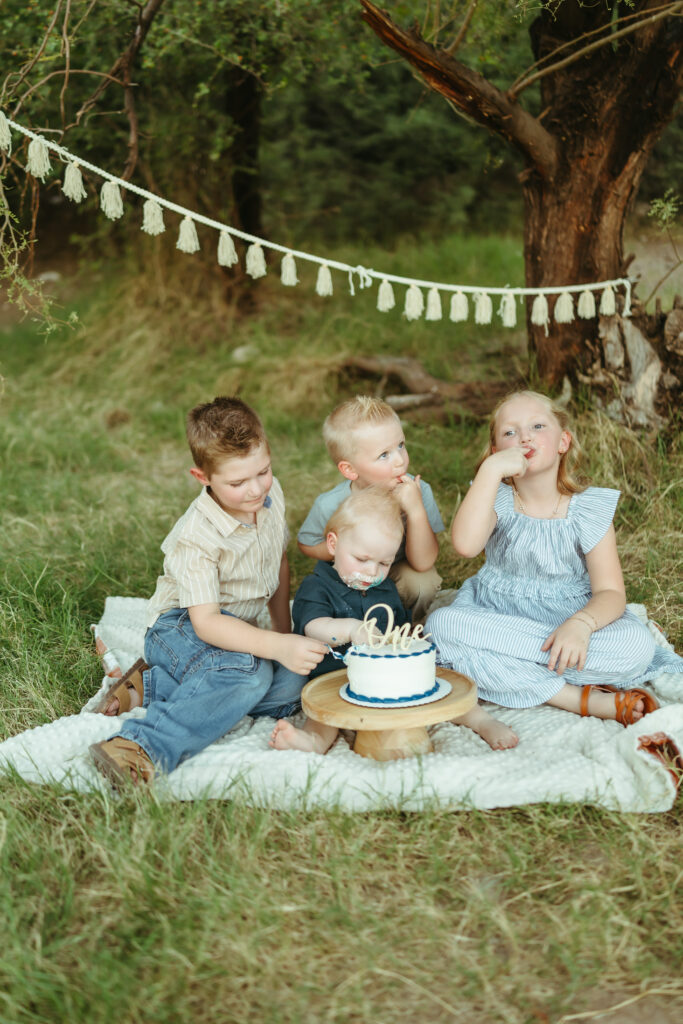 Four siblings celebrating their baby brother's first birthday with an outdoor cake smash photography session at Butcher Jones in Mesa, AZ.