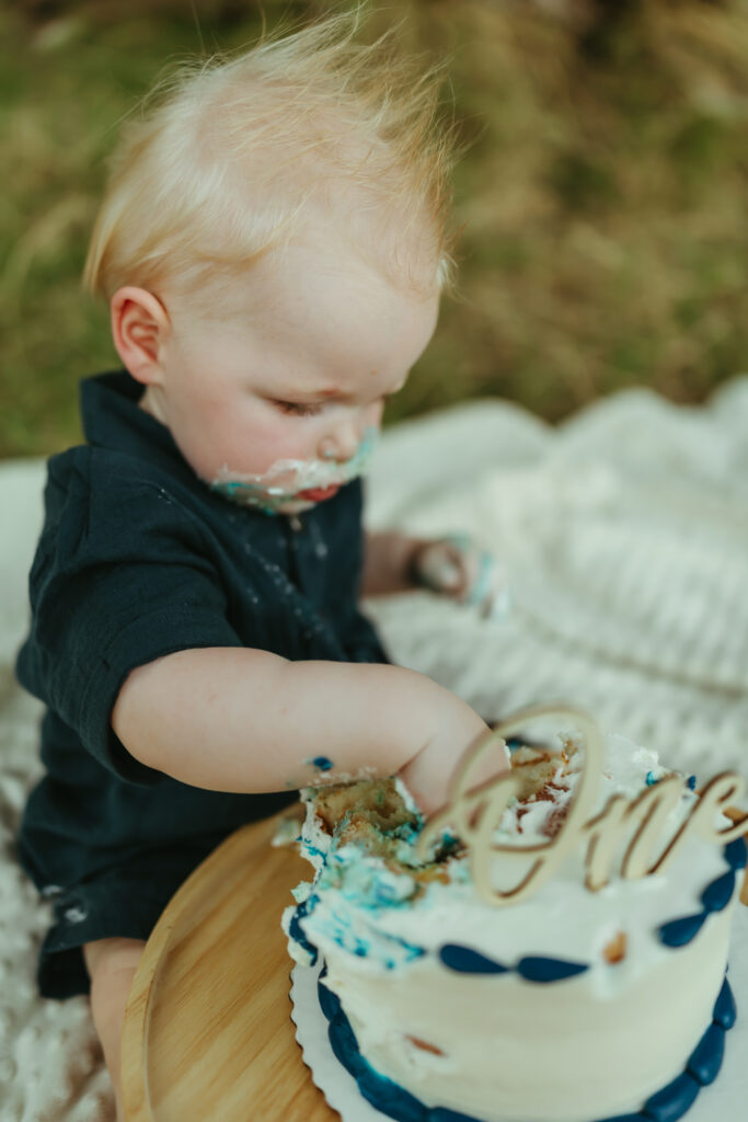 Close-up of a one-year-old boy digging into his birthday cake during an outdoor cake smash photo session near Saguaro Lake in Mesa, Arizona.